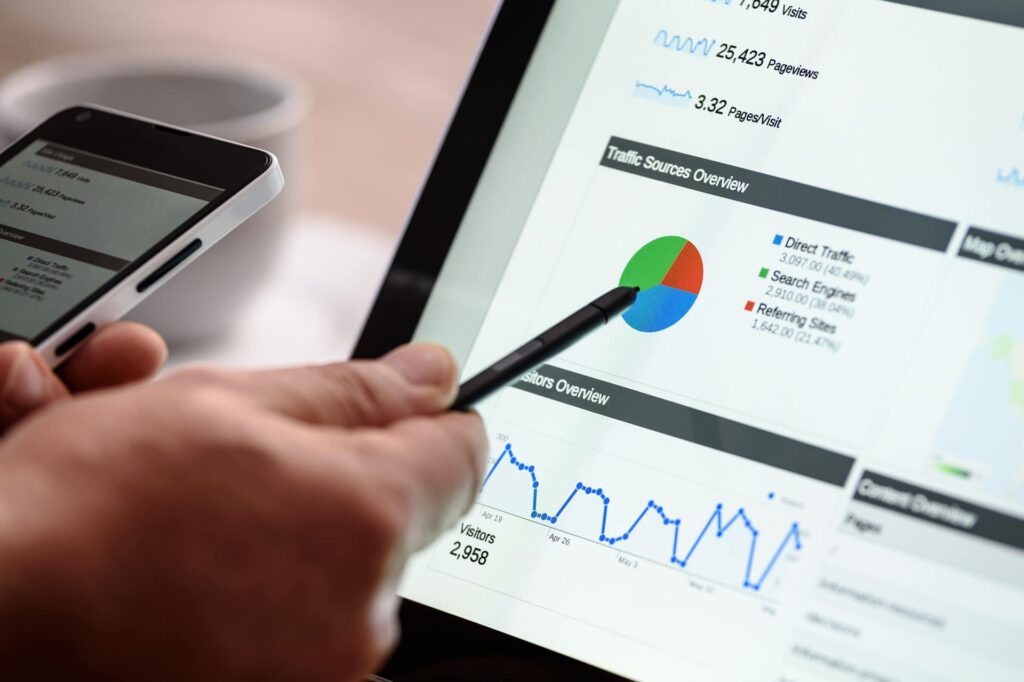 Close-up of a person reviewing website analytics on a tablet, pointing at a colorful traffic pie chart and line graph while holding a smartphone.